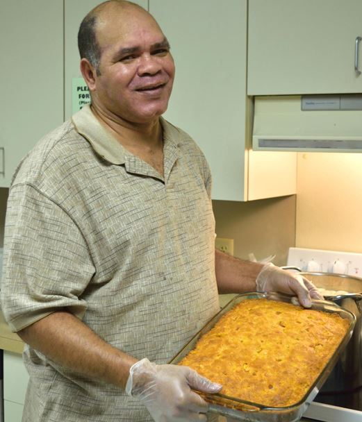 Man smiling at camera while holding a pan of freshly baked cornbread